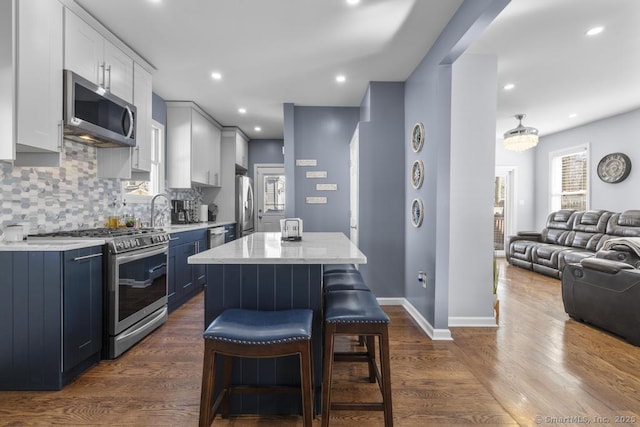 kitchen with blue cabinetry, a center island, appliances with stainless steel finishes, a kitchen breakfast bar, and white cabinets