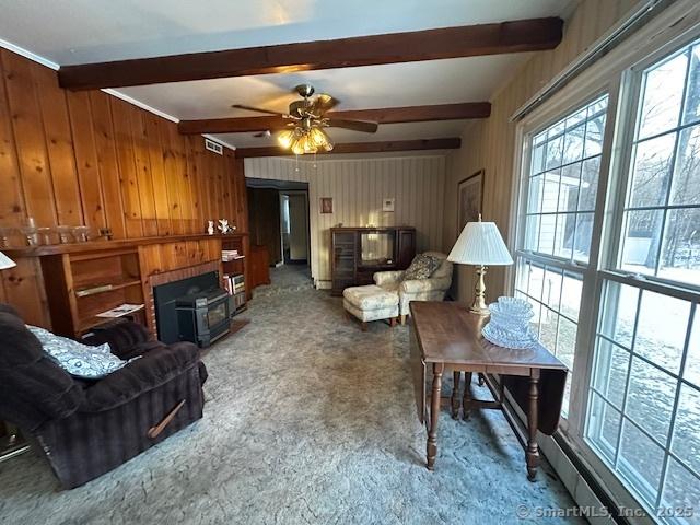 living room with beam ceiling, wood walls, ceiling fan, and carpet