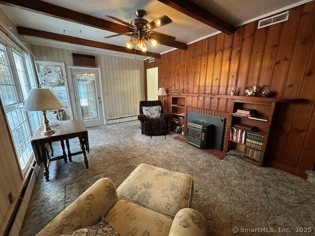 living area with baseboard heating, wooden walls, dark carpet, beamed ceiling, and ceiling fan