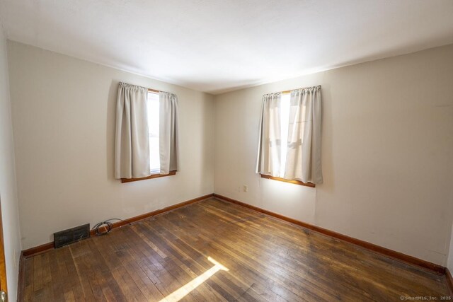 spare room featuring a healthy amount of sunlight and dark hardwood / wood-style flooring