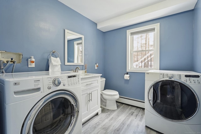 washroom with a baseboard heating unit, washer and clothes dryer, sink, and light hardwood / wood-style floors