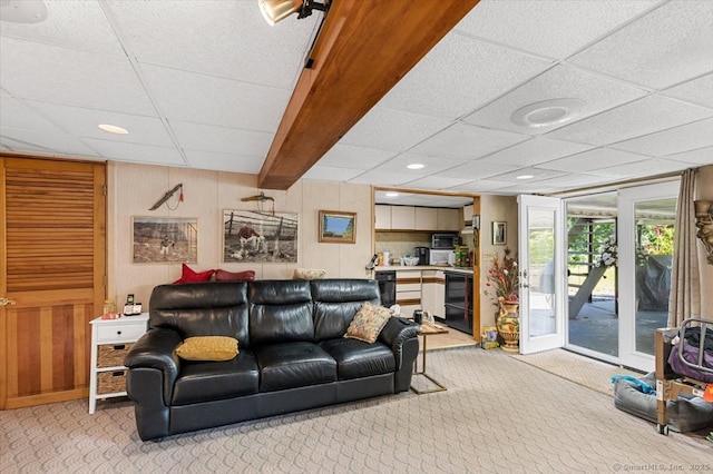 living room with light carpet, a drop ceiling, and wood walls