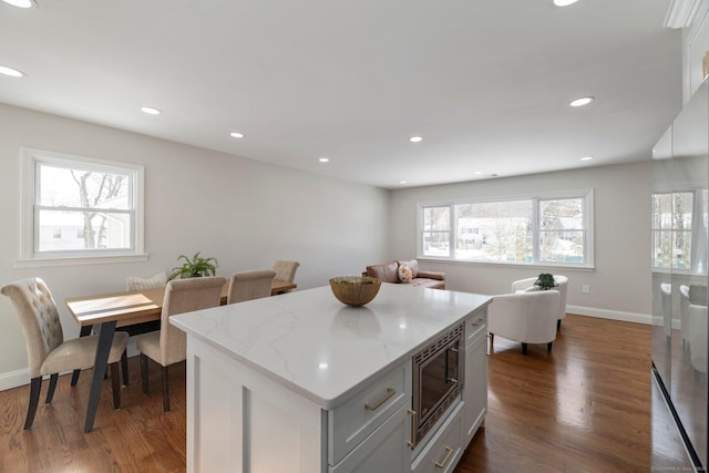 kitchen with stainless steel microwave, light stone counters, dark wood-type flooring, and a healthy amount of sunlight