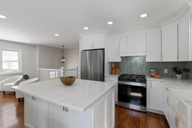 kitchen featuring appliances with stainless steel finishes, a kitchen island, white cabinetry, hanging light fixtures, and light stone counters