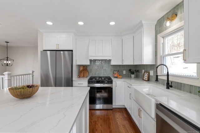 kitchen featuring appliances with stainless steel finishes, decorative light fixtures, white cabinetry, sink, and light stone countertops