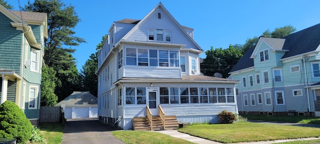 victorian house featuring a garage, a sunroom, an outbuilding, and a front lawn