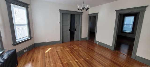 empty room with an inviting chandelier, radiator, and hardwood / wood-style floors