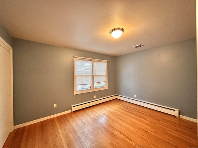 empty room featuring a baseboard heating unit and wood-type flooring