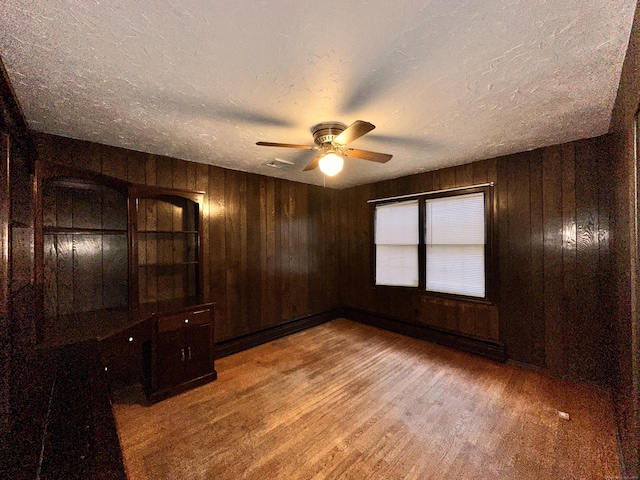 empty room featuring hardwood / wood-style floors, wooden walls, a textured ceiling, and ceiling fan