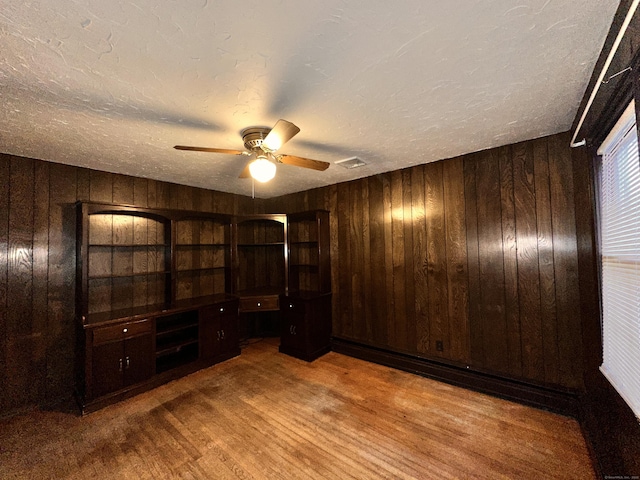 unfurnished room with hardwood / wood-style flooring, ceiling fan, a textured ceiling, and wooden walls