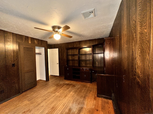 interior space with wood-type flooring, ceiling fan, a textured ceiling, and wood walls