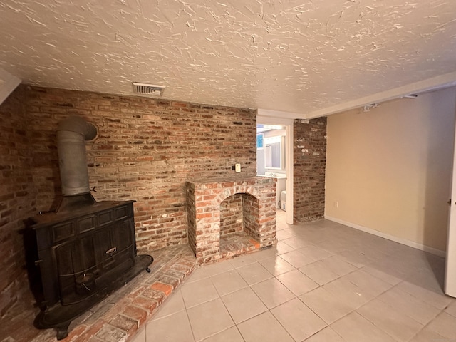 unfurnished living room featuring brick wall, a wood stove, light tile patterned floors, a brick fireplace, and a textured ceiling