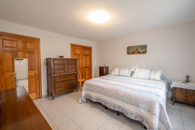 bedroom featuring light tile patterned floors, a textured ceiling, and white refrigerator