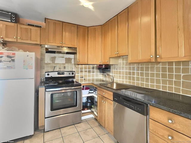 kitchen with light tile patterned floors, sink, appliances with stainless steel finishes, tasteful backsplash, and dark stone counters