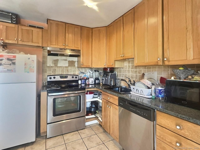 kitchen with tasteful backsplash, sink, dark stone countertops, light tile patterned floors, and stainless steel appliances