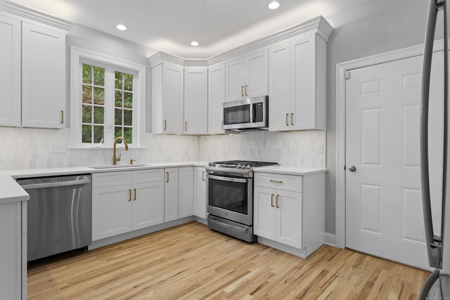 kitchen with appliances with stainless steel finishes, sink, white cabinets, and light hardwood / wood-style floors