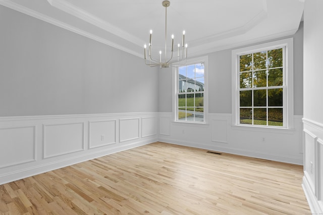 unfurnished dining area with an inviting chandelier, ornamental molding, a tray ceiling, and light hardwood / wood-style floors