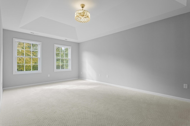 carpeted empty room with a notable chandelier and a tray ceiling