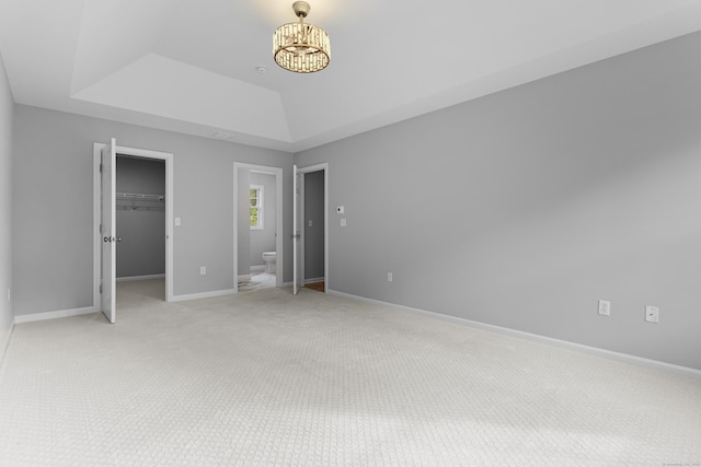 unfurnished bedroom featuring a walk in closet, a chandelier, light carpet, a raised ceiling, and a closet