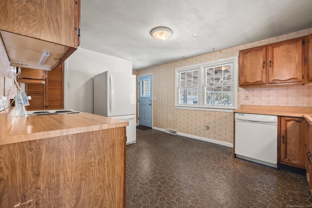 kitchen with dark floors, white appliances, baseboards, brown cabinetry, and wallpapered walls