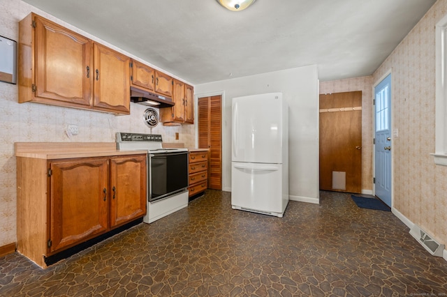 kitchen featuring wallpapered walls, brown cabinetry, electric stove, freestanding refrigerator, and under cabinet range hood