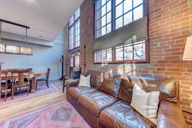 living room featuring hardwood / wood-style flooring, brick wall, and a high ceiling