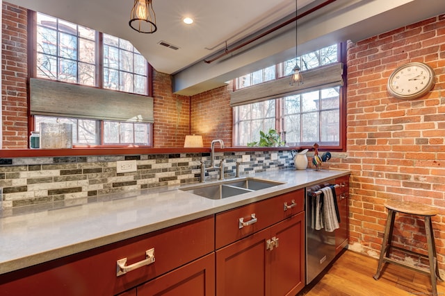 kitchen with sink, decorative light fixtures, light hardwood / wood-style flooring, stainless steel dishwasher, and brick wall