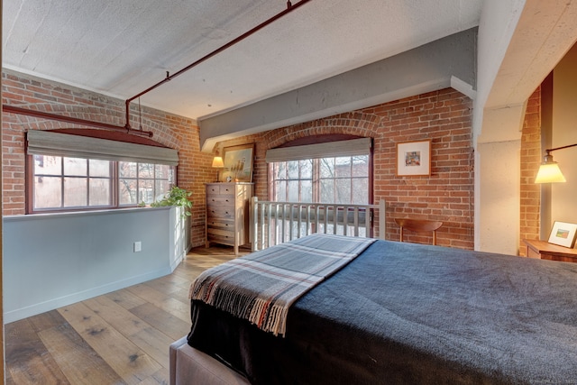 bedroom featuring brick wall, light hardwood / wood-style floors, multiple windows, and a textured ceiling