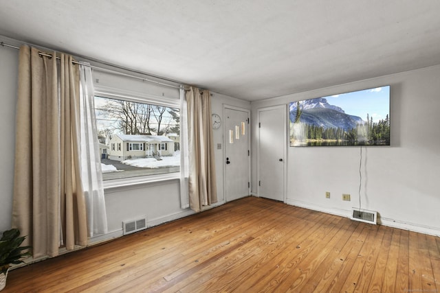 unfurnished room with wood-type flooring, visible vents, and baseboards