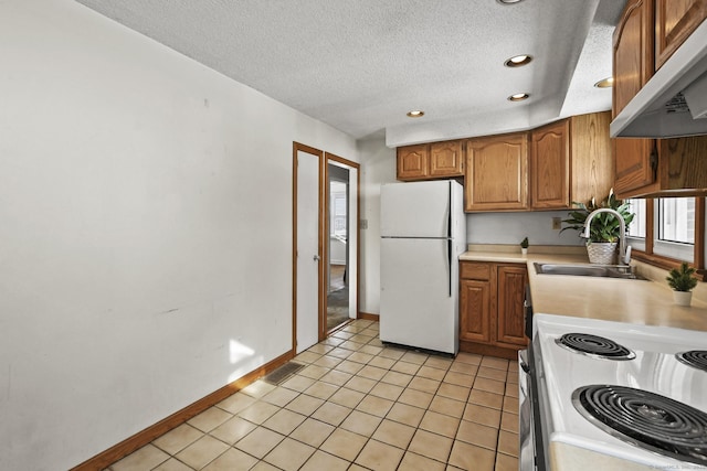 kitchen featuring under cabinet range hood, range with electric cooktop, a sink, light countertops, and freestanding refrigerator