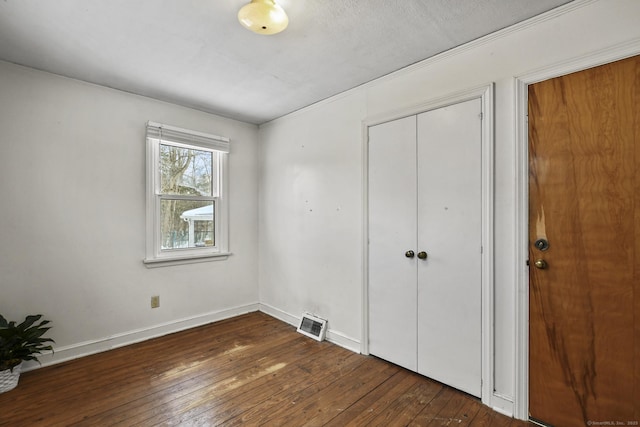 unfurnished bedroom with dark wood-style floors, visible vents, baseboards, and a closet