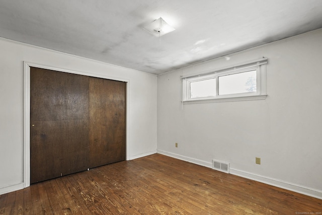 unfurnished bedroom featuring a closet, wood-type flooring, visible vents, and baseboards