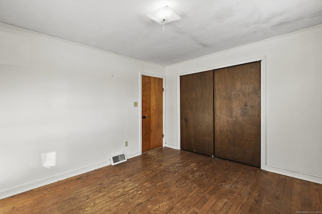 unfurnished bedroom with visible vents, a closet, hardwood / wood-style flooring, and baseboards