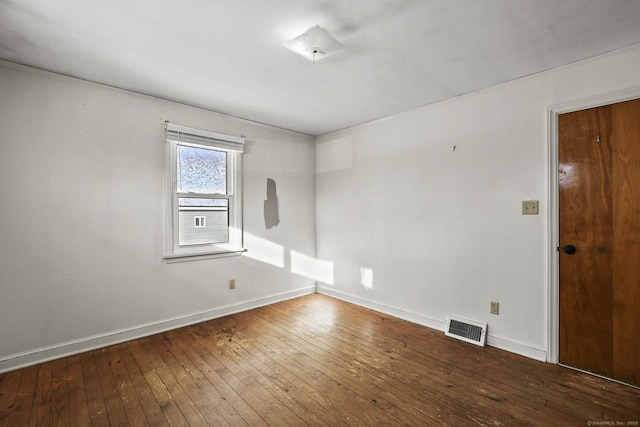 empty room with baseboards, visible vents, and hardwood / wood-style floors