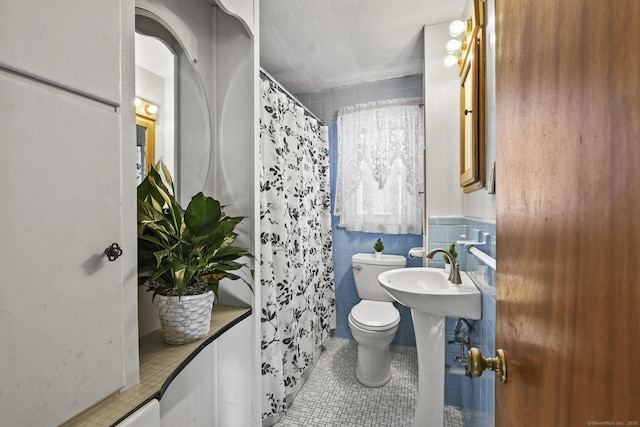 full bathroom featuring tile walls, a shower with shower curtain, toilet, a sink, and tile patterned flooring