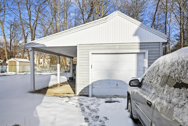 snow covered garage featuring a carport and a detached garage