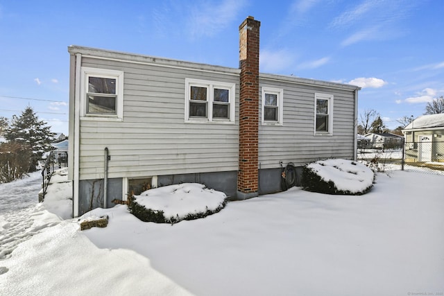 snow covered back of property featuring fence and a chimney