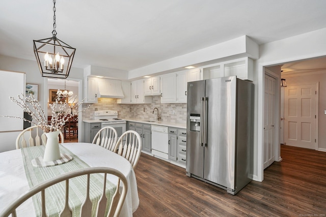 kitchen featuring dark wood-type flooring, hanging light fixtures, a notable chandelier, white appliances, and decorative backsplash