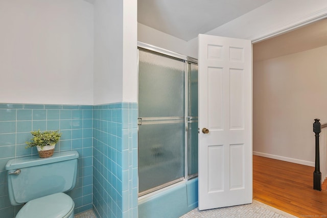 bathroom featuring combined bath / shower with glass door, tile walls, tile patterned floors, and toilet