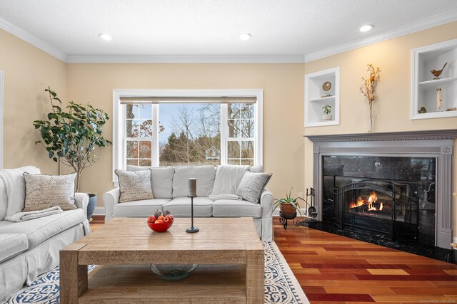 living room with hardwood / wood-style flooring, ornamental molding, a premium fireplace, and built in shelves