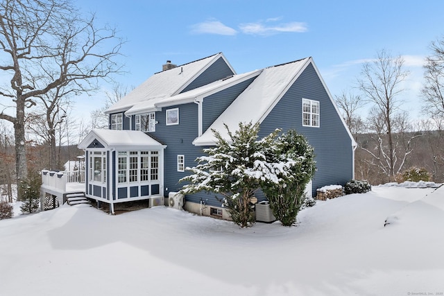 snow covered property with a wooden deck and a sunroom