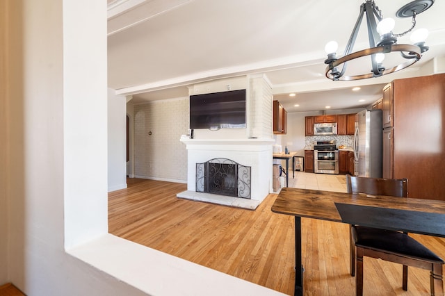 interior space featuring tasteful backsplash, stainless steel appliances, an inviting chandelier, and light wood-type flooring