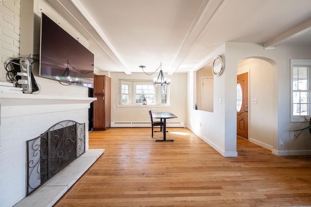 living room featuring beamed ceiling, a wealth of natural light, a fireplace, and light hardwood / wood-style flooring