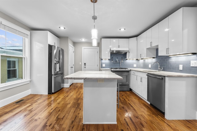 kitchen featuring appliances with stainless steel finishes, white cabinetry, a kitchen breakfast bar, a kitchen island, and decorative light fixtures