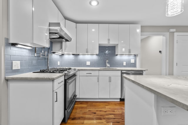 kitchen featuring wall chimney range hood, sink, appliances with stainless steel finishes, white cabinetry, and decorative light fixtures