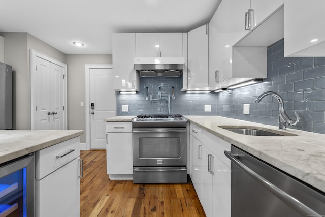 kitchen featuring wine cooler, sink, ventilation hood, appliances with stainless steel finishes, and white cabinets