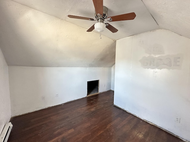 additional living space featuring vaulted ceiling, a textured ceiling, dark hardwood / wood-style flooring, ceiling fan, and a baseboard heating unit