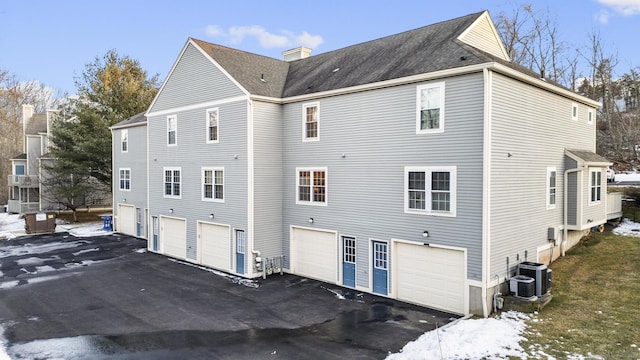 snow covered rear of property featuring cooling unit and a garage