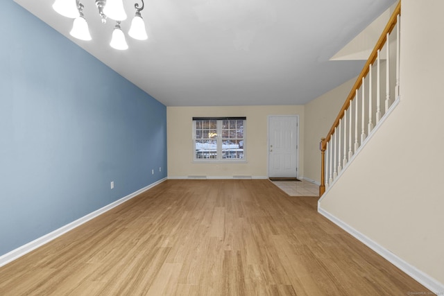 unfurnished living room with an inviting chandelier and light hardwood / wood-style flooring