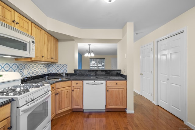 kitchen with hanging light fixtures, sink, dark stone countertops, and white appliances